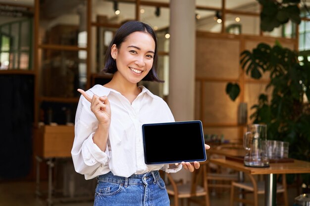 Smiling asian businesswoman demonstrating showing tablet screen and pointing at banner advertising