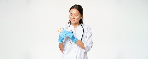 笑顔のアジアの医師は、滅菌手袋で薬を保持しているビタミンを宣伝する医療薬を示しています