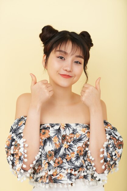 Smiling Asian girl in bare shoulder top posing in studio with thumbs up