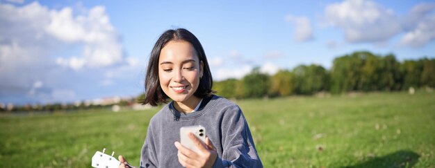 Smiling asian girl looking at guitar app singing and playing ukulele while peeking at chords on