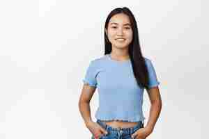 Free photo smiling asian girl standing in blue tshirt looking confident and happy at camera standing over white background