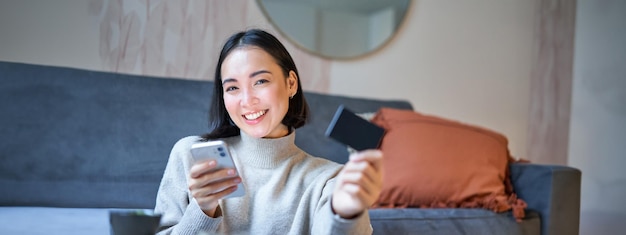 무료 사진 스마트폰과 신용카드를 들고 웃고 있는 아시아 소녀는 휴대폰을 사용하여 온라인 쇼핑을 합니다.