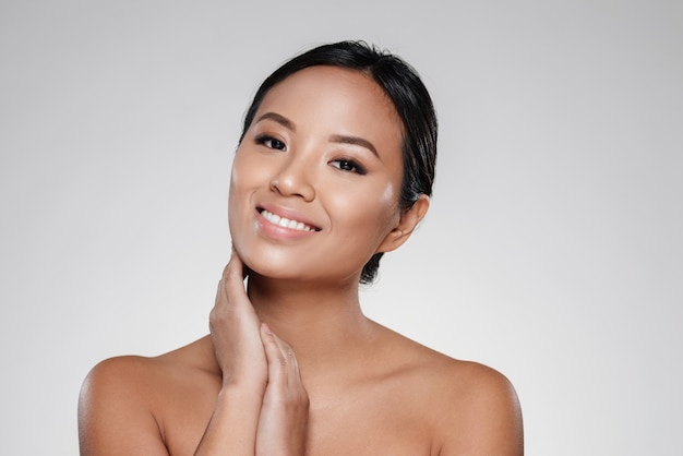 Smiling asian lady touching her clear skin and looking camera