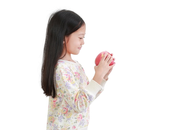 빨간 사과를 손에 들고 흰색 배경 위에 그것을 보고 웃고 있는 아시아 소녀. 측면보기