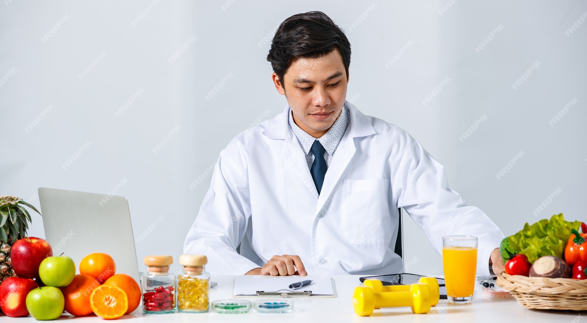 Premium Photo | Smiling asian male nutritionist sitting at table with  assorted fresh fruits and looking at lablet computer while showing concept  of healthy diet