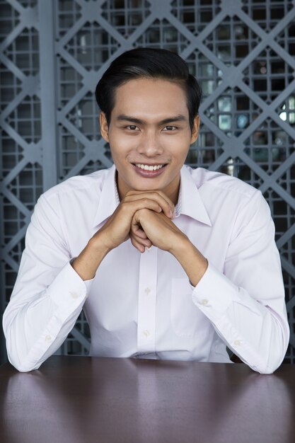 Smiling Asian Man Sitting with Hands Under Chin