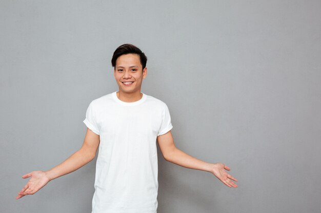 Smiling asian man standing over grey wall.