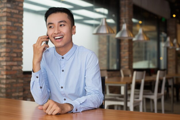 Smiling Asian Man Talking on Phone at Cafe Table