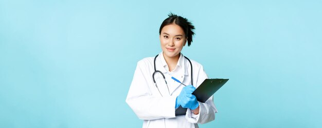 Smiling asian medical worker female physician writing down patient info holding pen and clipboard st