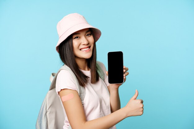 Smiling asian tourist shows arm with patch from covid vaccination showing coronavirus vaccine intern...