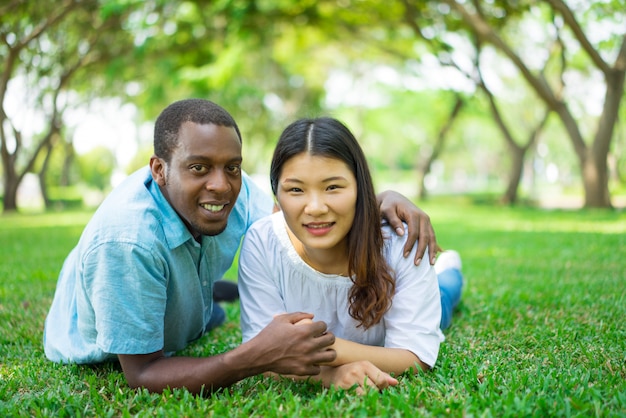 Smiling Asian woman and African American man lying on grass. 