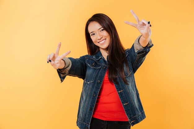 Smiling asian woman in denim jacket showing peace gestures