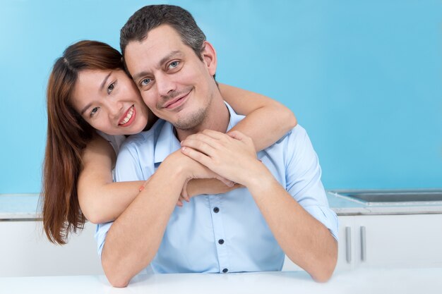 Smiling Asian Woman Embracing Husband in Kitchen