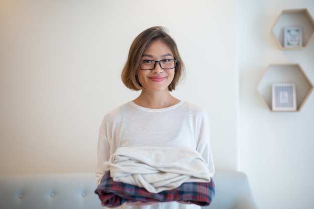 Smiling Asian woman holding clean folded clothes at home