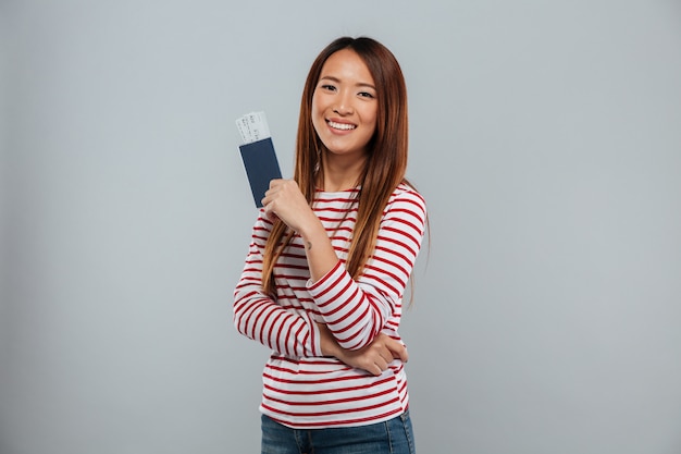 Smiling asian woman in sweater holding passport with tickets