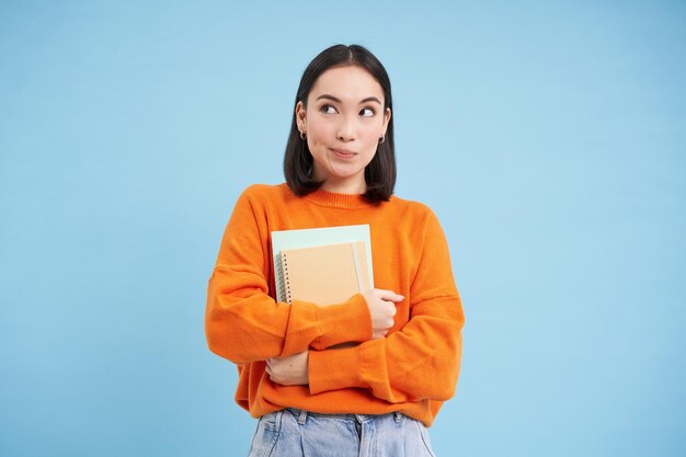 Smiling asian woman with notebooks student with happy face promo of college education blue backgroun