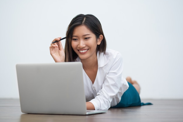 Sorridente donna asiatica di lavoro sul computer portatile sul pavimento