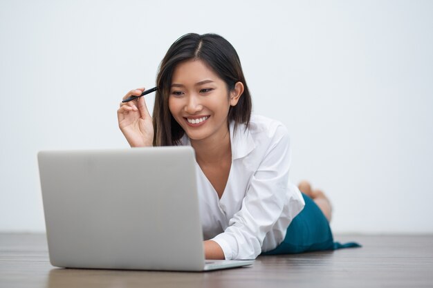 Улыбается Азии женщина работает на ноутбуке на полу