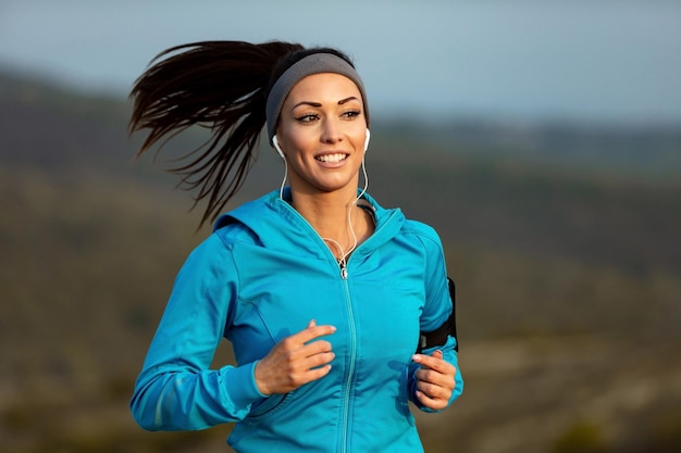 Smiling athletic woman jogging in the morning and listening music over earphones