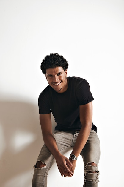 빈 검은 면화 t- 셔츠와 청바지 흰 벽에 앉아 운동 젊은 아프리카 계 미국인 남자 웃 고