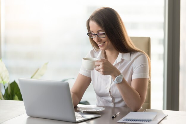 Smiling attractive businesswoman drinking invigorating coffee during break at workplace 