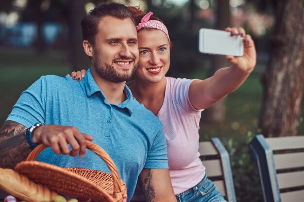 Smiling attractive couple taking selfie at a picnic in a park, during dating outdoors.