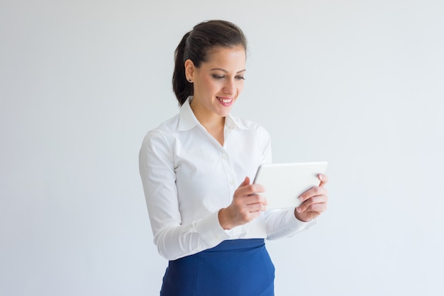 Smiling attractive female manager in white shirt using device.