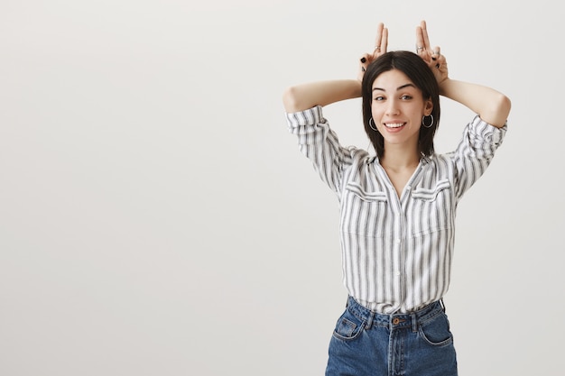 Foto gratuita sorridente ragazza attraente che mostra il gesto delle corna, essendo testardo