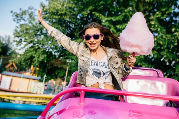 Sorridente ragazza attraente in occhiali da sole in sella a montagne russe per bambini