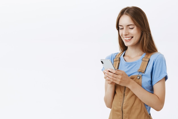 Sorridente ragazza attraente utilizzando il telefono cellulare, sms o navigazione nei social network