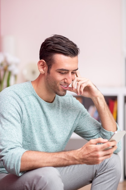 Smiling Attractive Man Using Smartphone at Home