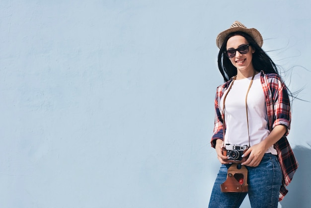 smiling attractive woman holding camera standing against blue wall