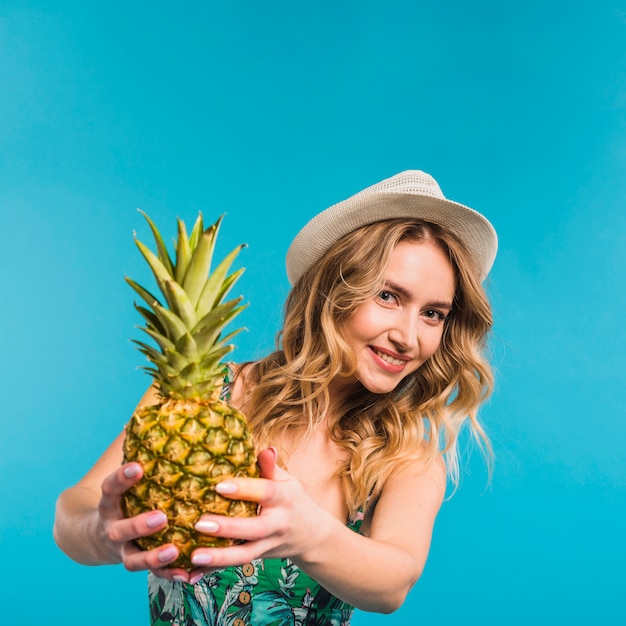 Giovane donna attraente sorridente in cappello che tiene ananas fresco