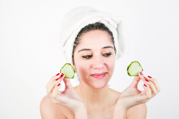 Smiling attractive young woman holding cucumber slices in hand against white background