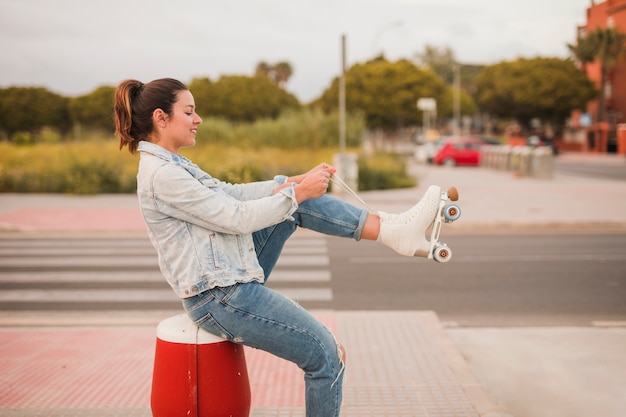 무료 사진 롤러 스케이트 레이스를 묶는 거리에 앉아 웃는 매력적인 젊은 여자