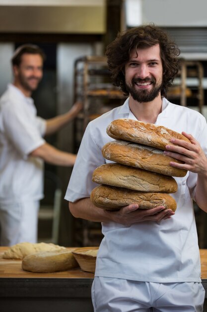 Smiling baker carrying stack of baked breads