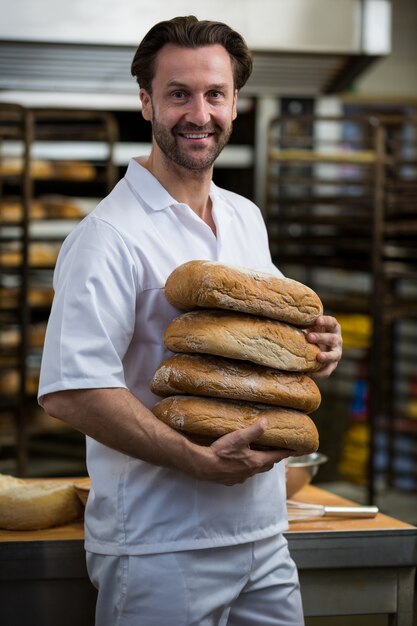 Smiling baker carrying stack of baked breads