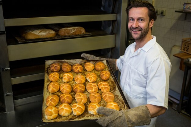 Smiling baker carrying a tray of baked buns