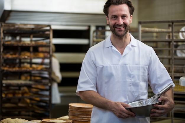 Smiling baker holding a bowl and a whisk