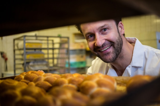 Free photo smiling baker removing baked bun from oven