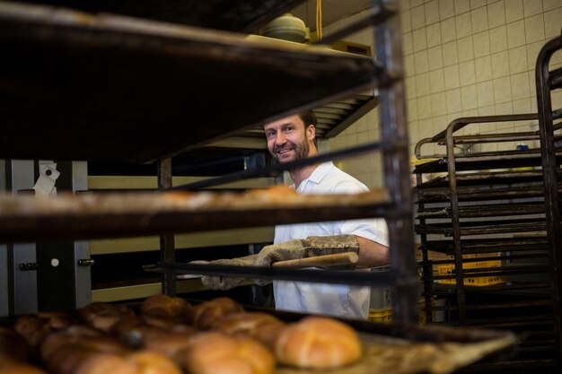 Smiling baker removing baked bun from oven