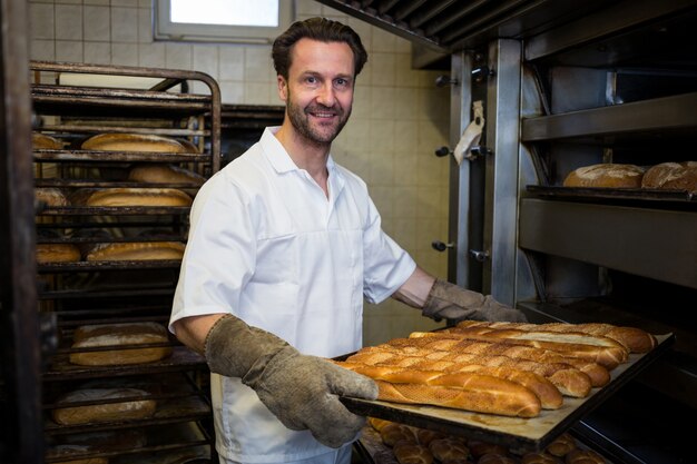 Smiling baker removing baked buns from oven
