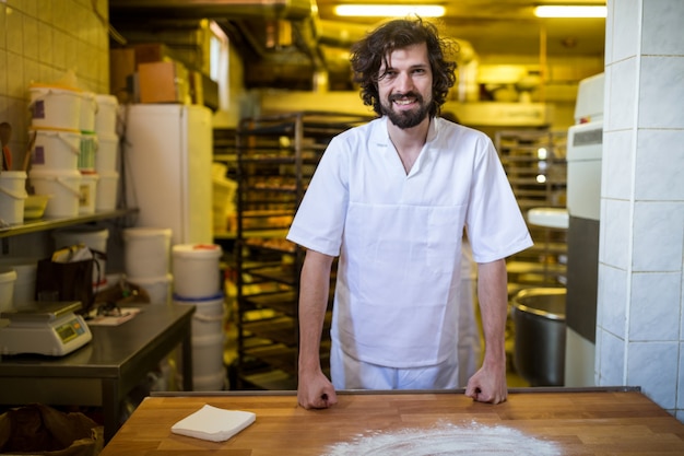 Foto gratuita sorridente panettiere in piedi al banco di lavoro