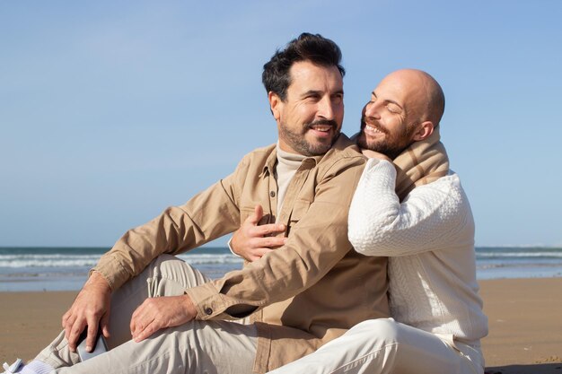 Smiling bald man sitting on sand with boyfriend