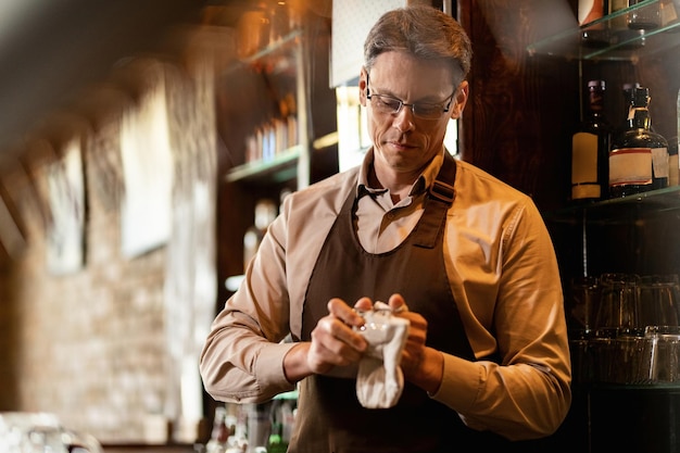 Smiling barista cleaning drinking glass while working behind bar counter