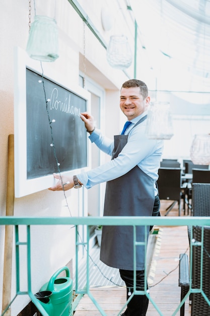 Smiling barman writing on chalkboard at terrace