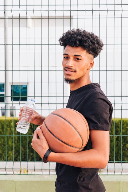 Giocatore di pallacanestro sorridente con la bottiglia di acqua che esamina macchina fotografica