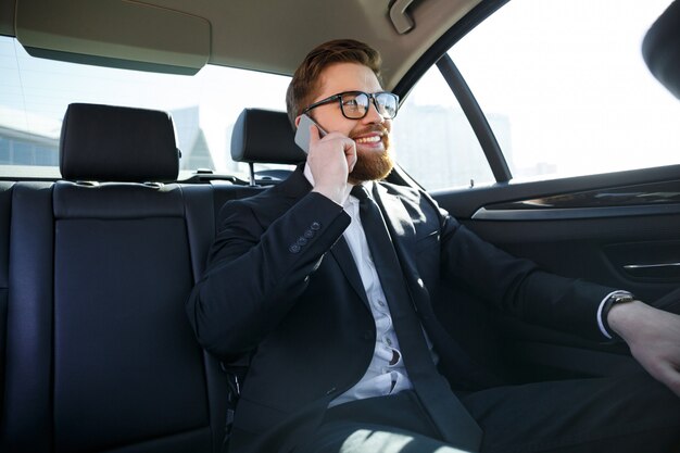 携帯電話で話している眼鏡のひげを生やしたビジネス男の笑みを浮かべてください。