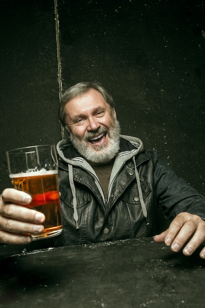 Бесплатное фото Улыбающийся бородатый мужчина пьет пиво в пабе