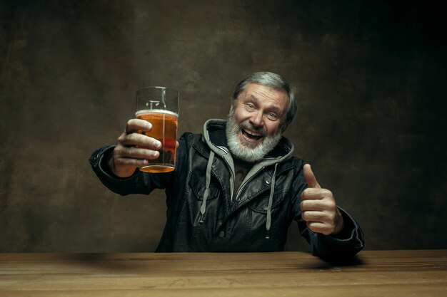 Улыбающийся бородатый мужчина пьет пиво в пабе